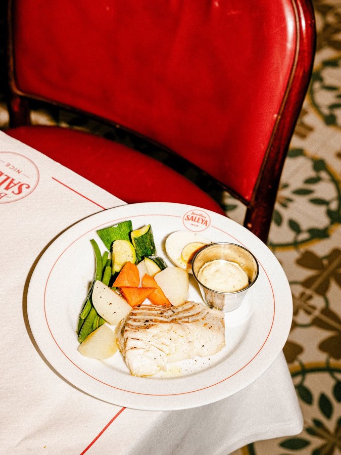 Une assiette au cachet du restaurant sur la nappe au liseré rouge, devant la banquette de cuir
