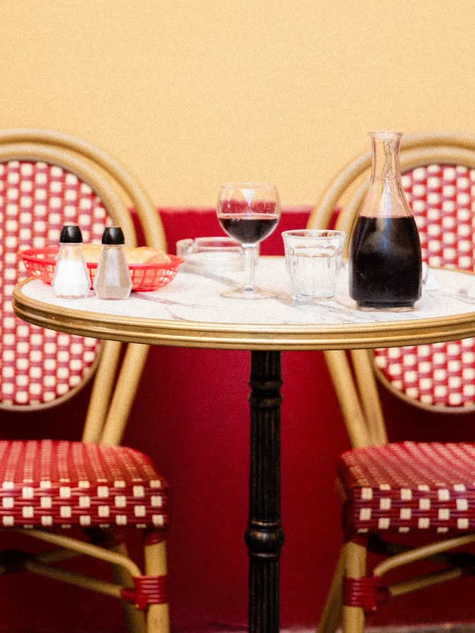 Table dressée entre deux chaises de bistrot au cannage rouge, carafe de vin